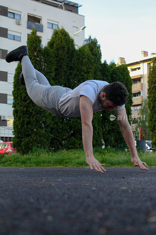 A white man jumping from the ground while doing a pushup in a public park